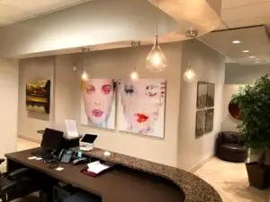 Regenerative Longevity: The Future of Preventative Medicine 4 A modern office reception area with a curved granite desk, computers, and papers hints at a professional space—perfect for consultations on stem cell therapy Dallas. Abstract portraits, pendant lights, and a potted plant add contemporary charm.