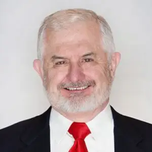 Regenerative Longevity: The Future of Preventative Medicine 3 A middle-aged man with short gray hair and a white beard is wearing a black suit jacket, white shirt, and red tie, smiling at the camera against a plain light background—an advocate for regenerative therapy and chronic pain treatment.