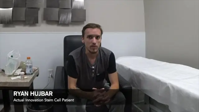 A man sits in a medical examination room beside a covered exam table. On the left, a Gatorade bottle, plastic bag, and items rest on a small table. Text reads, “RYAN HUJBAR Actual Innovation Stem Cell Patient undergoing regenerative therapy.”.